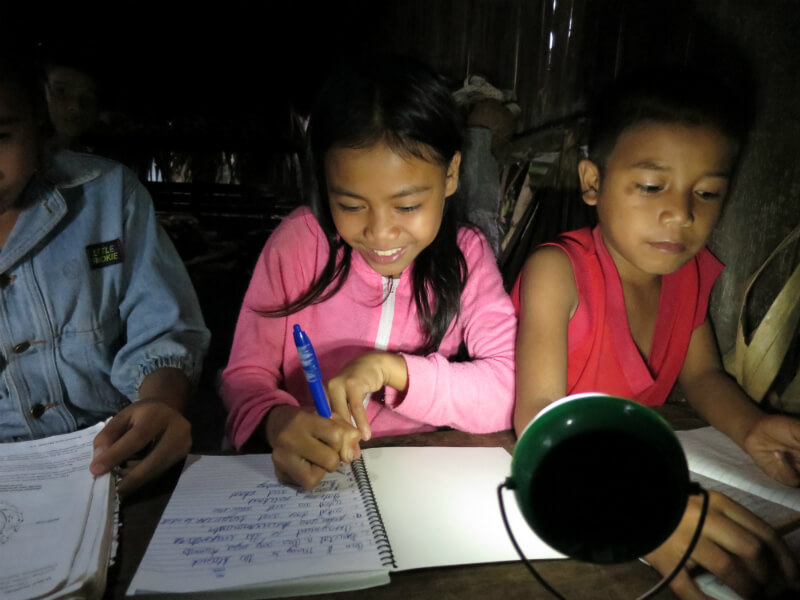 Filipino children study together at night with a portable solar light