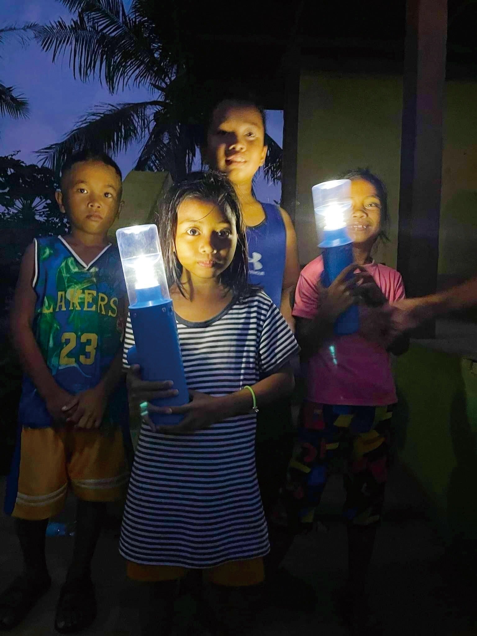Children in a remote Mindanao community hold portable solar lanterns at dusk